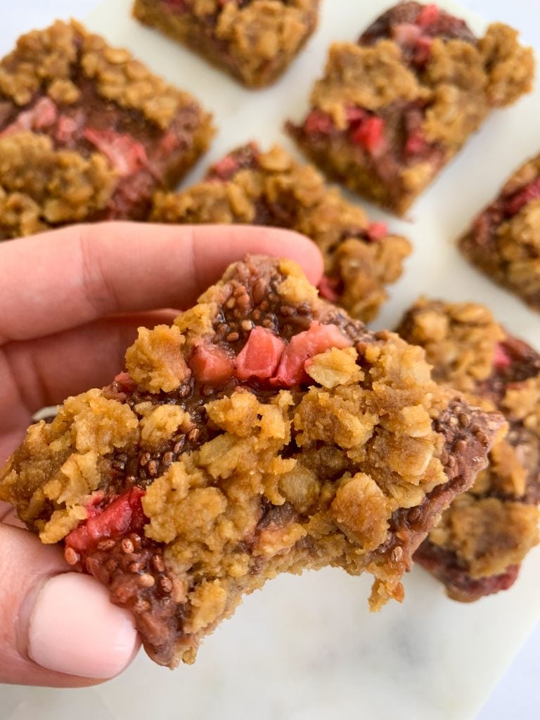 a hand holding a strawberry almond crumble cake bars over a white board