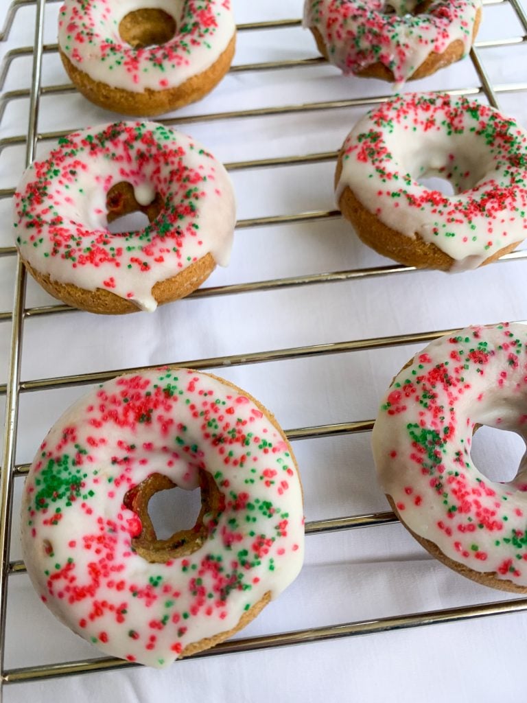 white chocolate holiday donuts on a cooling rack over a white sheet background