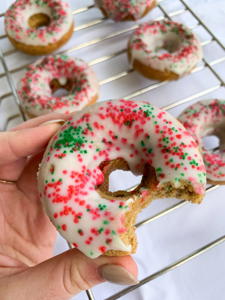 a hand holding one of the white chocolate holiday donuts over the rest of them
