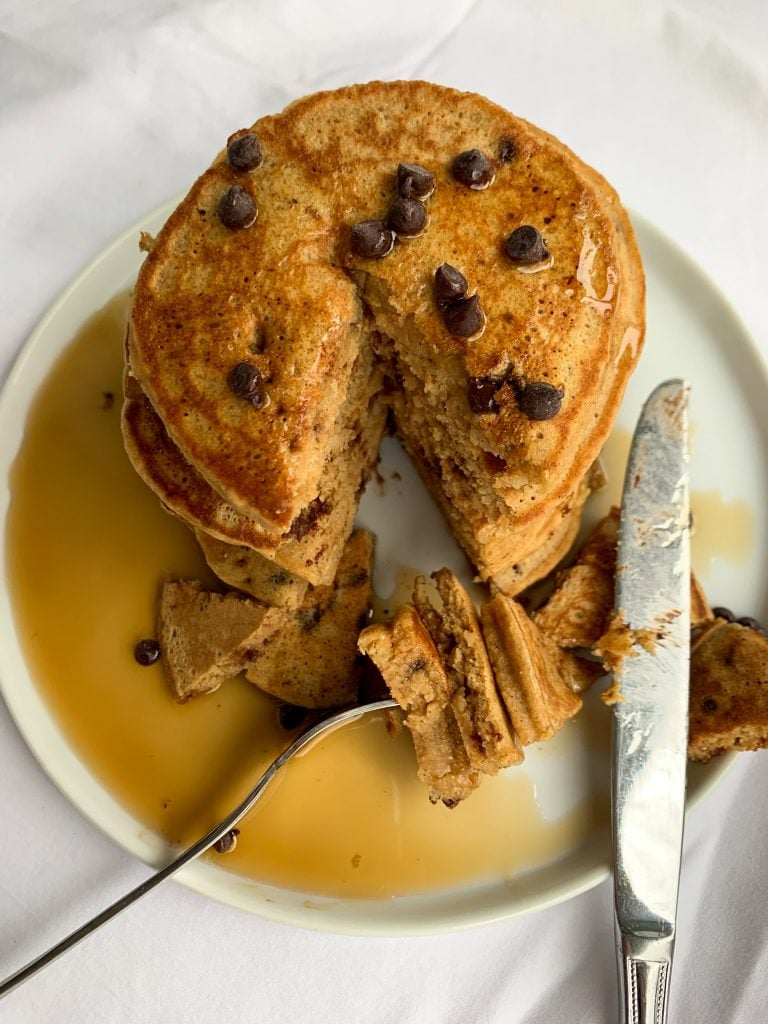 a stack of whole wheat chocolate chip pancakes with maple syrup and chocolate chips on top and a fork and knife
