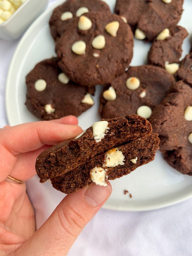 a hand holding one of the White Chocolate Chip Brownie Cookies split open to show the inside
