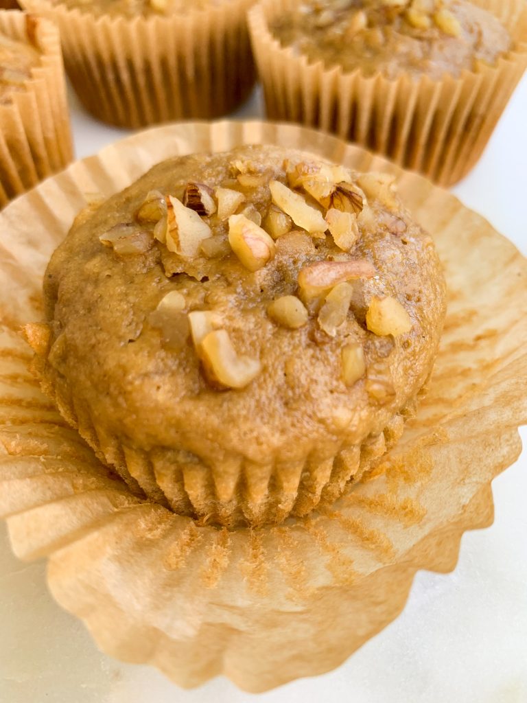 a close up of one whole wheat banana nut muffin on a white background