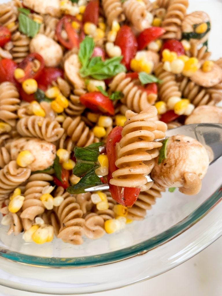 a fork with some pasta salad on it over a big bowl of the pasta salad