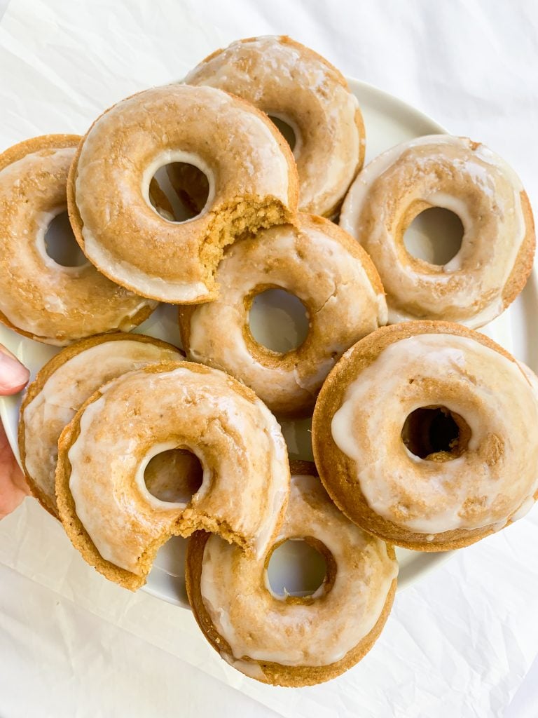 a hand holding a plate of healthy baked donuts over a white background