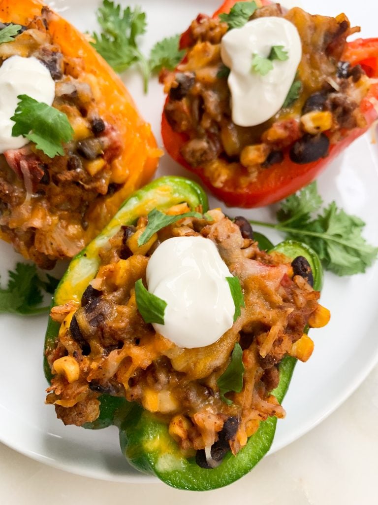 a white plate of Mexican stuffed peppers topped with sour cream and cilantro