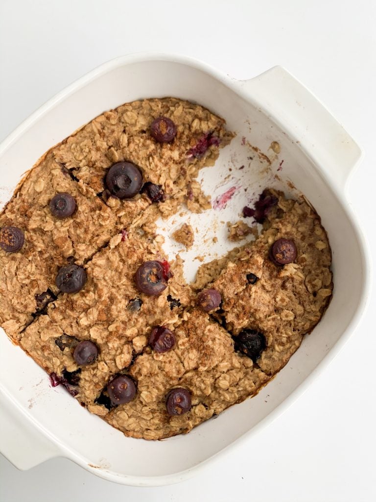overhead shot of peanut butter banana berry baked oatmeal in a white baking dish with one slice missing