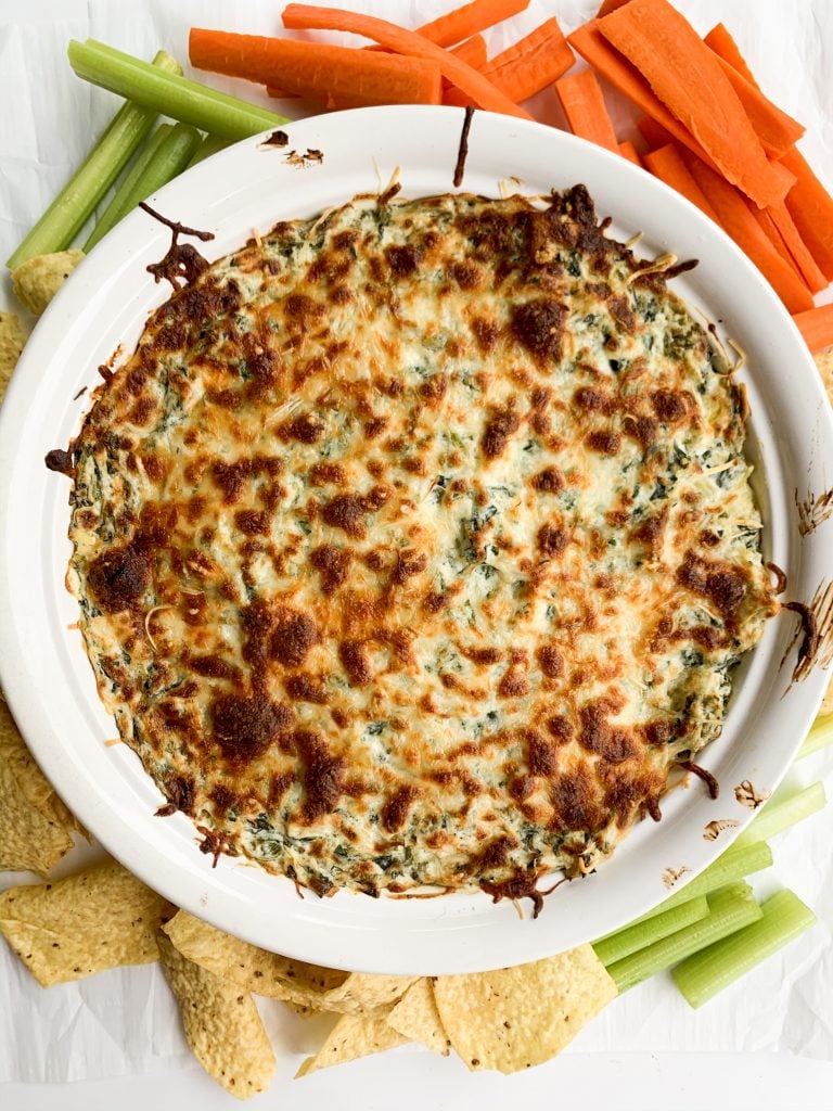 overhead shot of spinach dip in a round baking dish, surrounded by veggies and chips