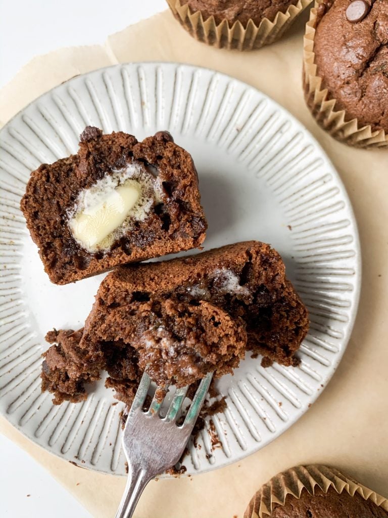 a plate with one chocolate zucchini muffin cut in half with butter on top 
