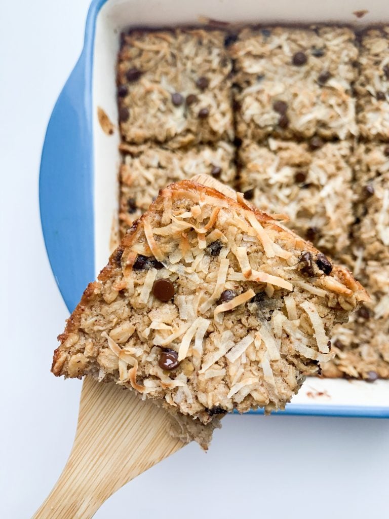 a close up of a oatmeal square on a wooden spatula being held over the dish with the rest of the oatmeal