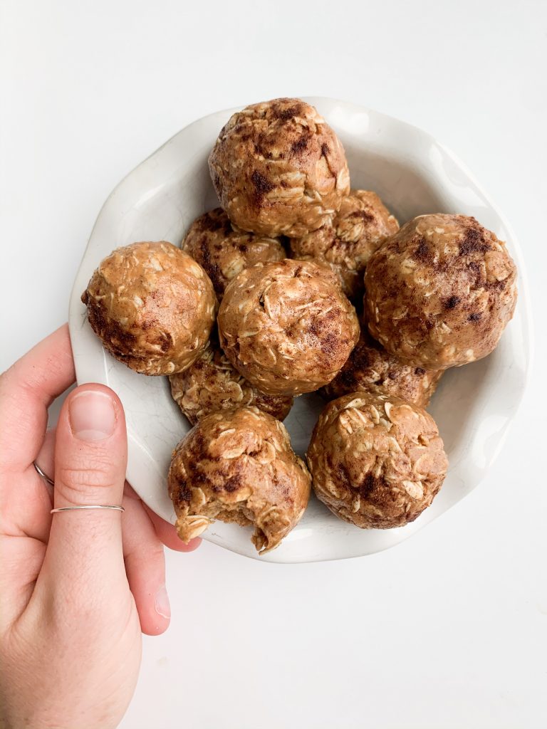 a white bowl of energy balls on a white background, hand holding the bowl