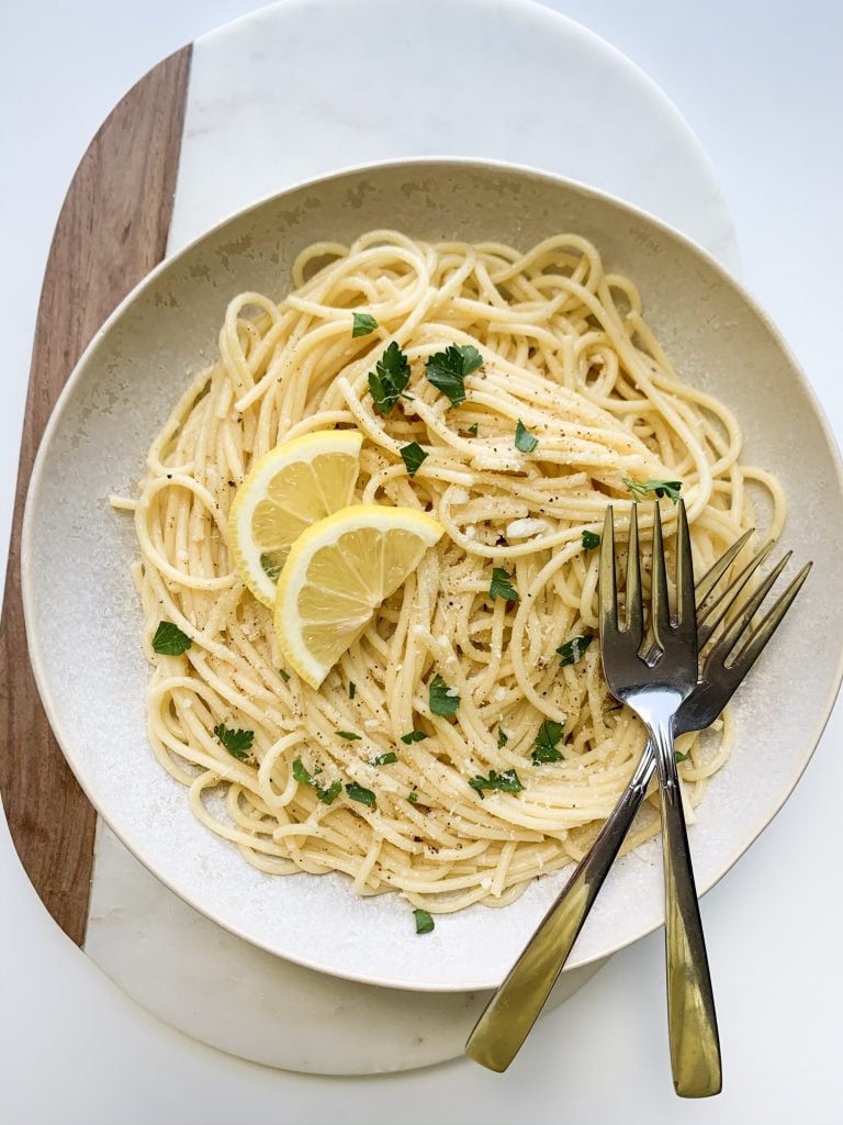 a bowl of spaghetti garnished with lemon slices and parsley, with two forks on top