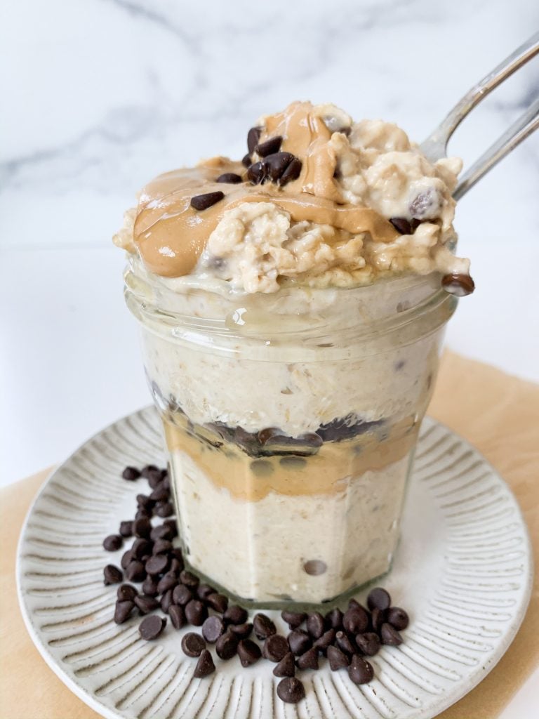 layered jar of oats on a plate surrounded by chocolate chips and with two spoons in the jar