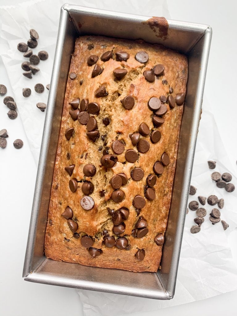 banana bread still in the loaf pan, on parchment paper, surrounded by chocolate chips