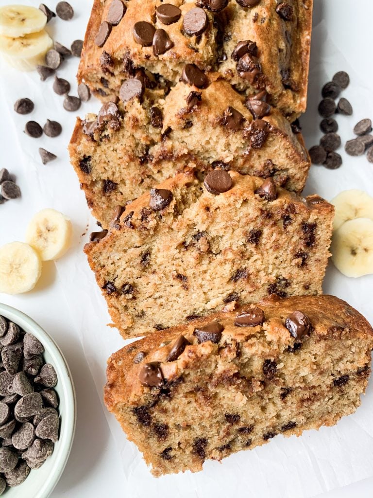banana bread on white background surrounded by chocolate chips and banana slices