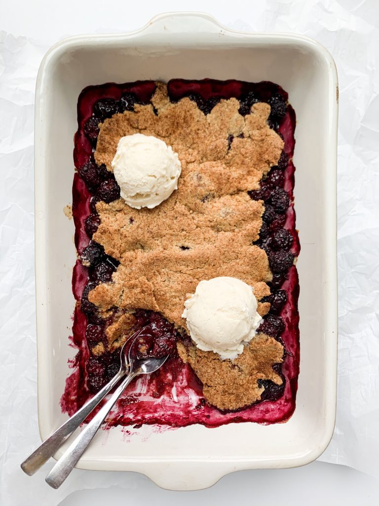 dish of blackberry cobbler with two scoops of vanilla ice cream and two spoons
