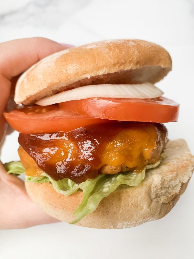 a hand holding a barbecue chicken burger over a white surface