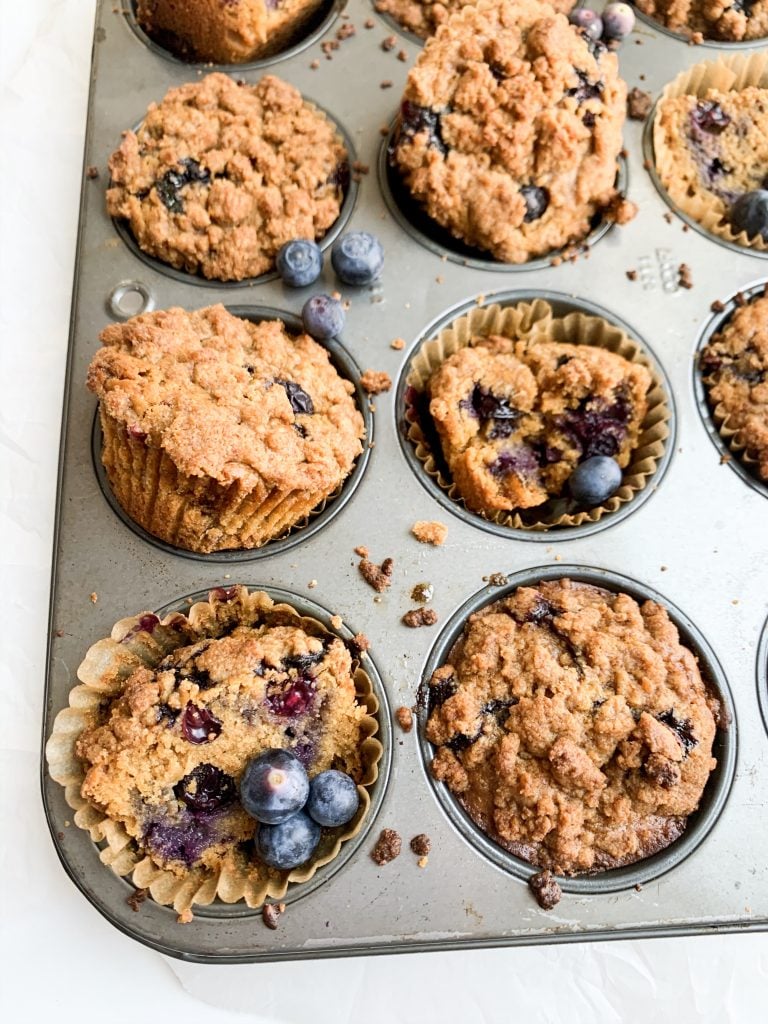 blueberry crumb muffins in a muffin tin with extra blueberries