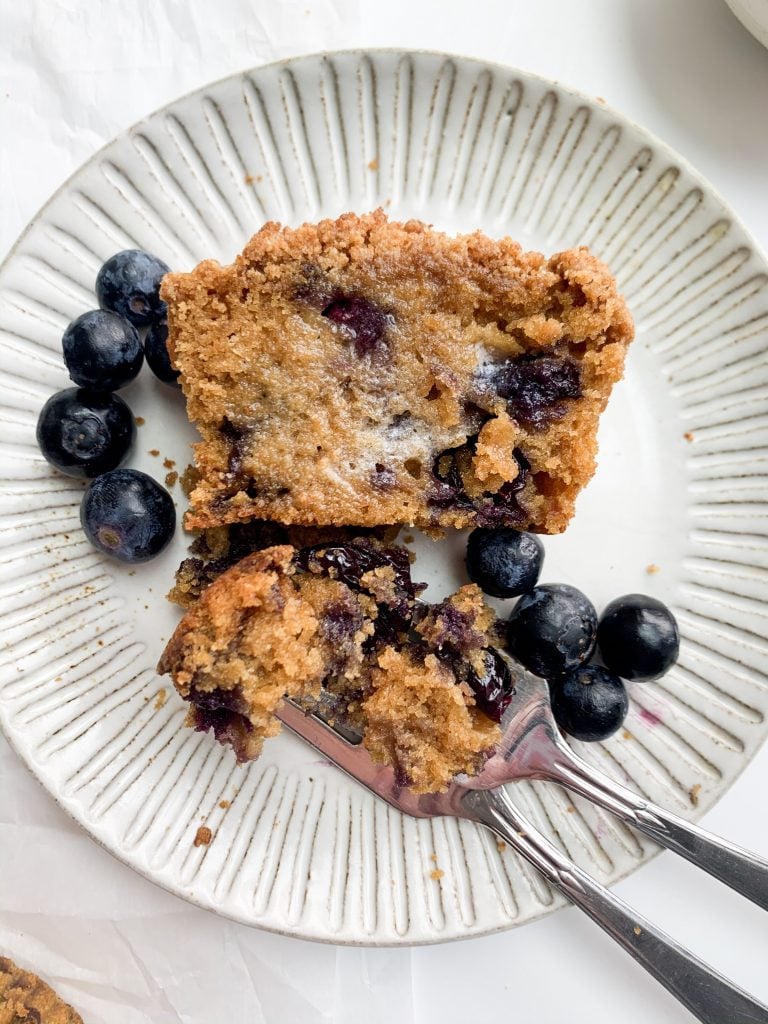 a muffin cut in half with melted butter on top and blueberries on the side