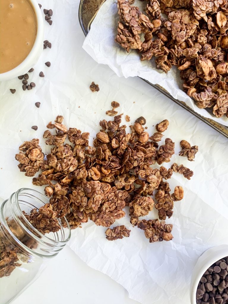 a jar of chocolate and peanut butter granola pouring onto a white background