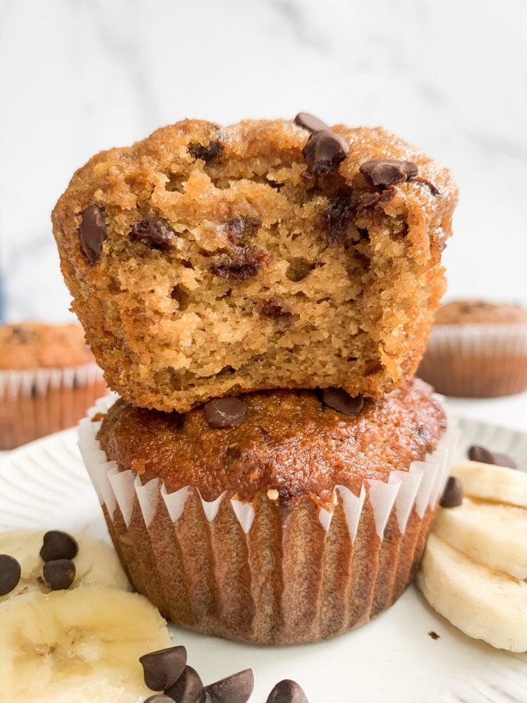 a stack of two banana muffins on a plate surrounded by banana slices and chocolate chips