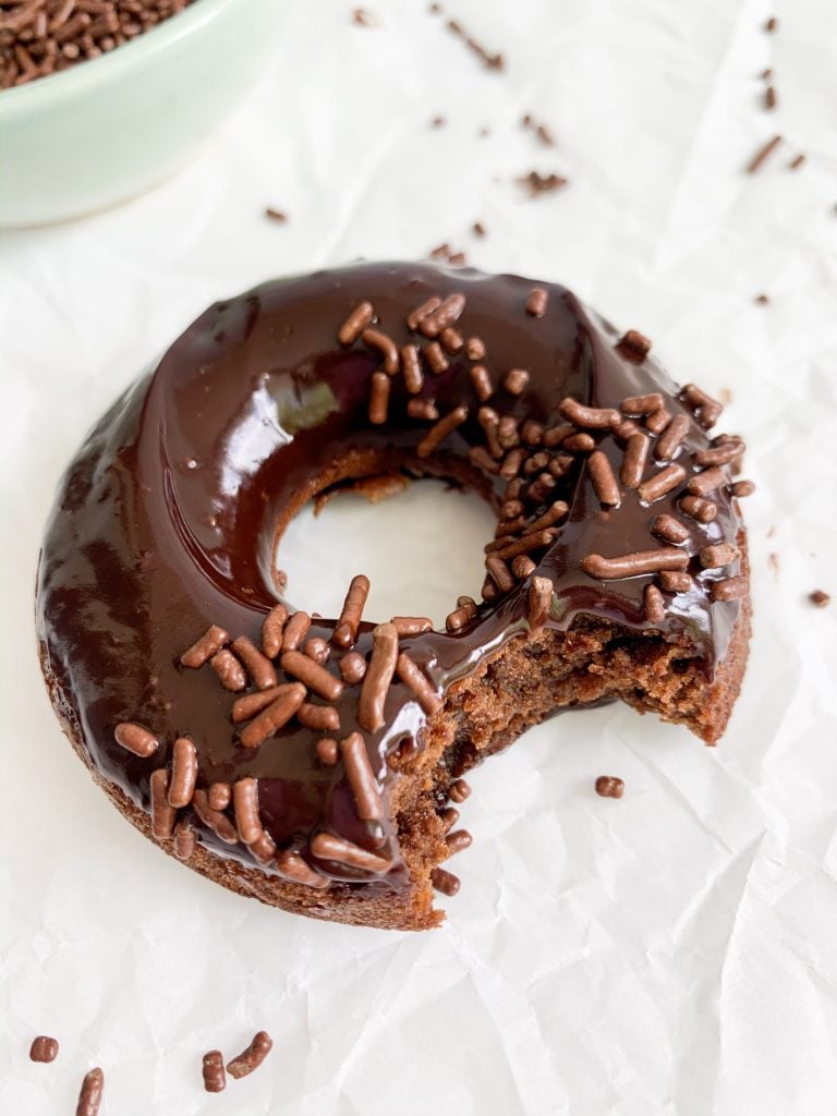 a chocolate baked donut on a white background with a bite taken out