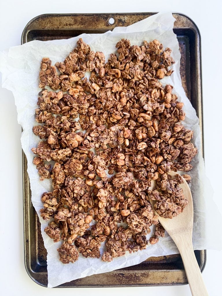 chocolate granola on  baking tray with a wooden spoon