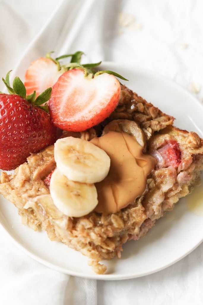 a slice of strawberry banana baked oatmeal with peanut butter & fruit on top