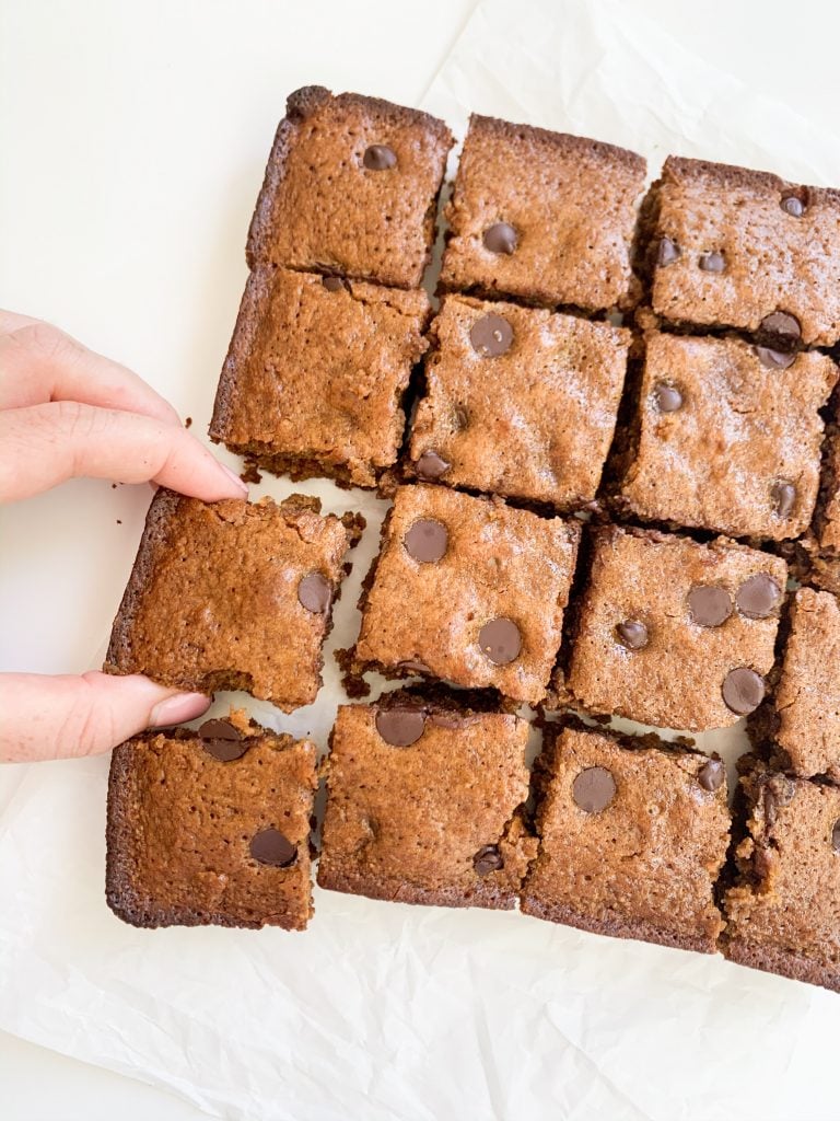 almond butter blondies on a white background with a hand taking one