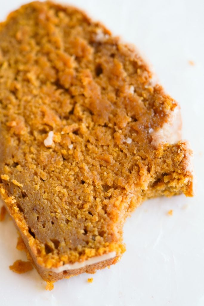 slice of Moist Pumpkin Bread with maple glaze laying on its side with a bite taken out.