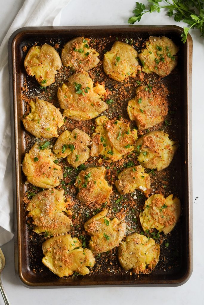 overhead shot of crispy garlic parmesan smashed potatoes on a baking tray on a white background
