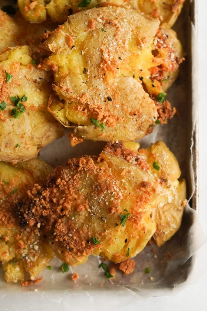 close up shot of smashed potatoes on a wax paper lined small baking tray