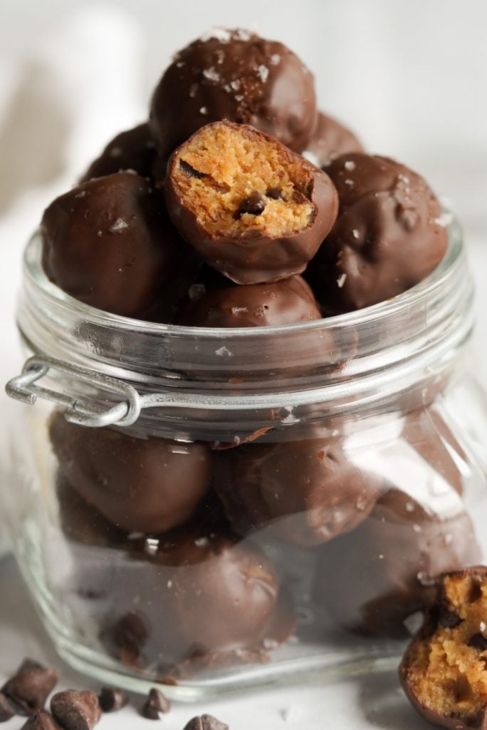 chocolate coated no bake cookie dough balls in a jar on a white background