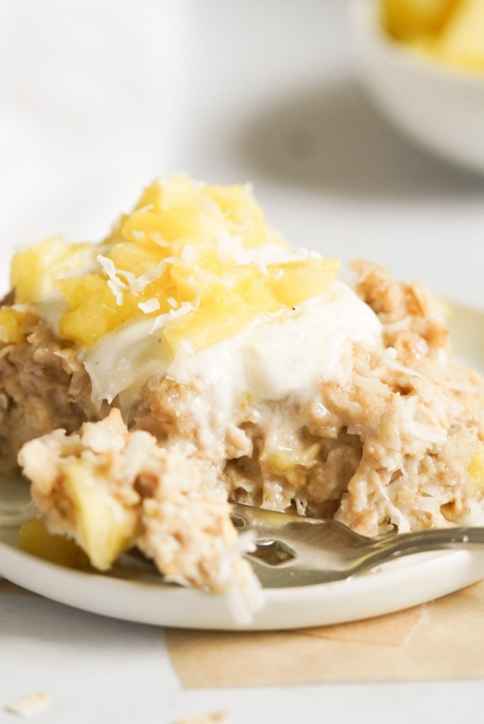 piece of oatmeal on a small plate with yogurt and pineapple on top, a bite being taken out with a fork