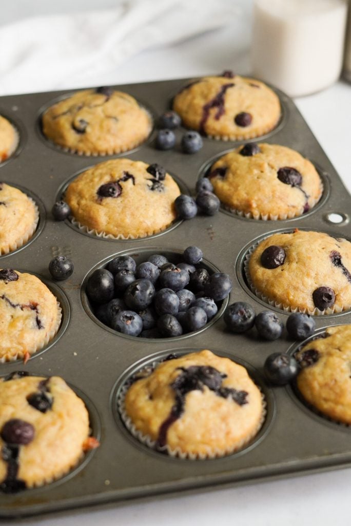 blueberry banana muffin tin with muffins still in it, one of the muffin holes is filled with blueberries