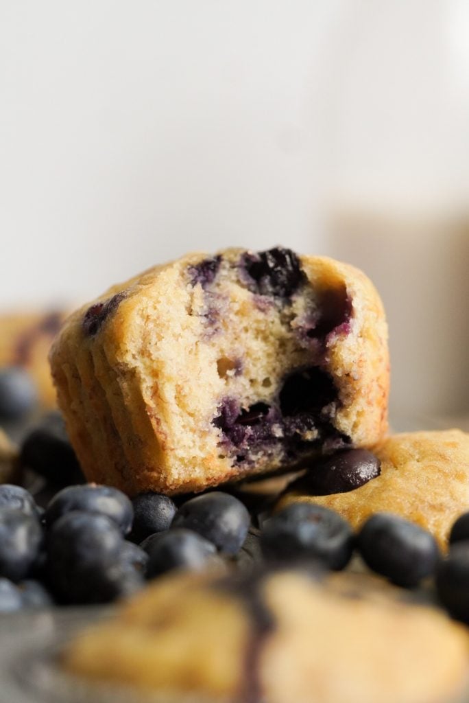 closeup shot of an easy blueberry banana muffin on top of the muffin pan with blueberries around it