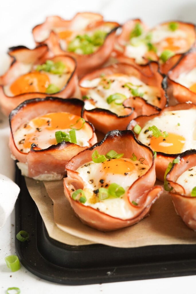 egg cups on parchment paper on a black tray topped with green onions