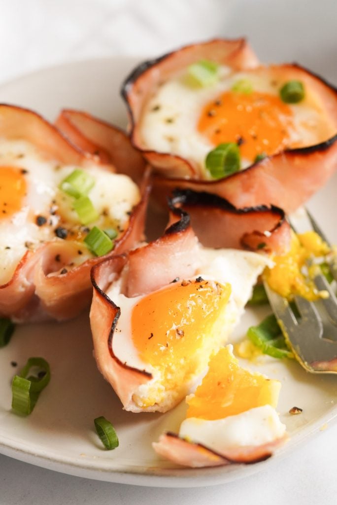 close up shot of three ham and cheese egg cups on a small plate, one is split in half 