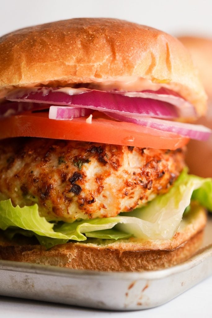 close up shot of a chicken burger on a bun with tomato, lettuce, and onion