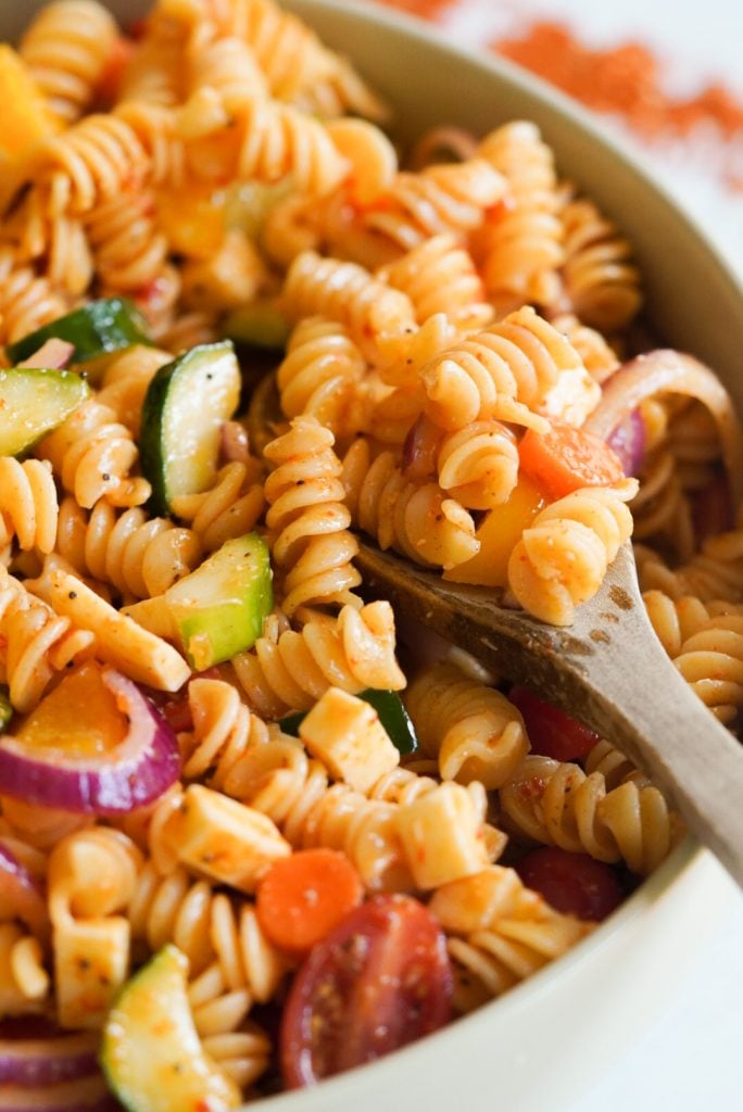 supreme pasta salad with a wooden spoon taking a spoonful