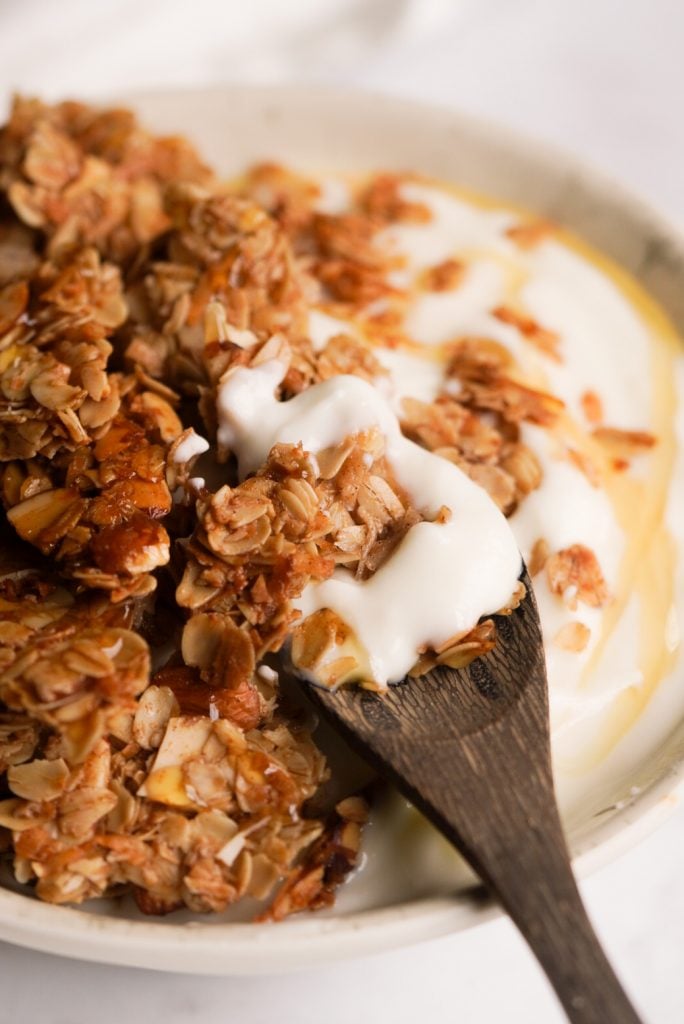 crunchy granola on top of a yogurt bowl with a spoon taking a bite