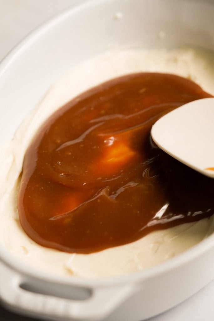 caramel dip being spread on top of cream cheese layer