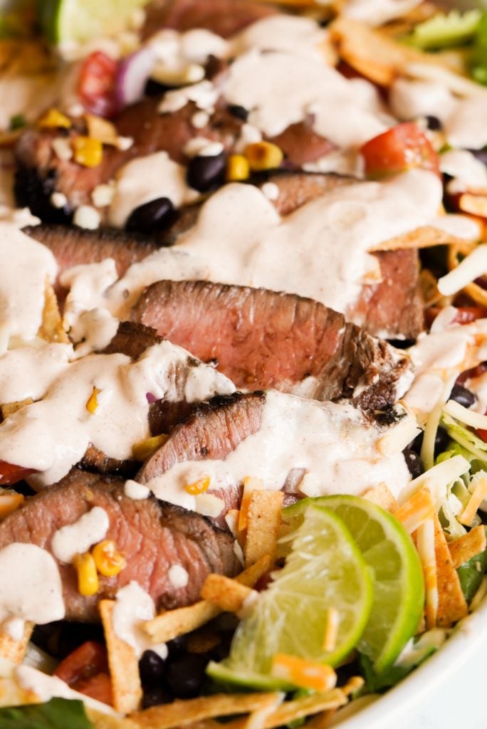 close up of salad with steak and creamy dressing on top