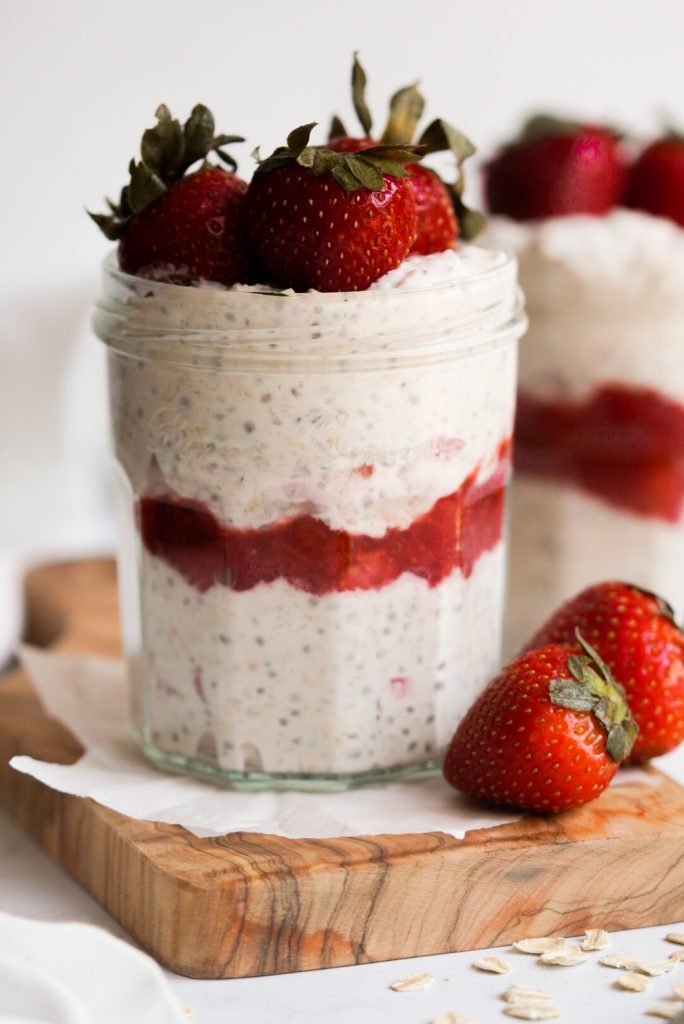 jar of overnight oats on a wooden board with strawberries on the side