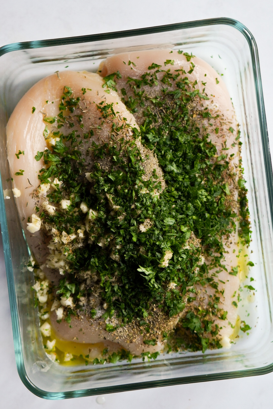 chicken breasts covered with the marinade ingredients - fresh herbs, olive oil, lemon juice