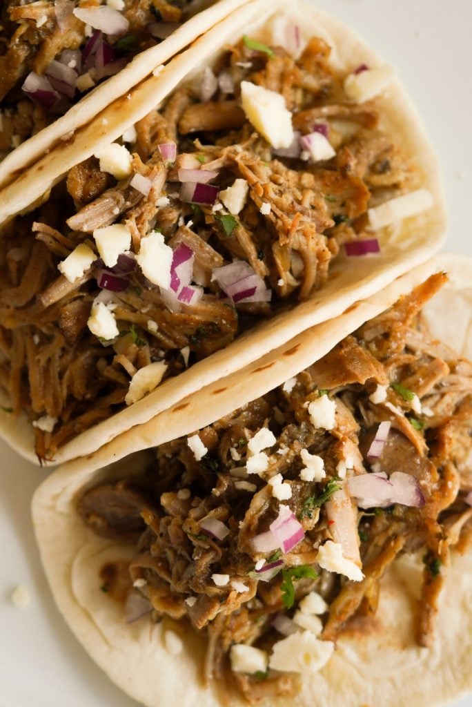 carnitas in a flour tortillas with cilantro, cotija cheese, and red onion