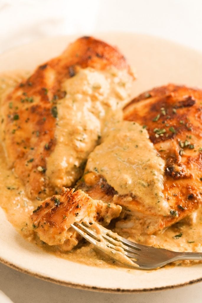 seared chicken breasts on plate covered in creamy herb sauce