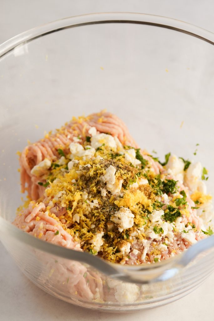 ground chicken, lemon zest, spices, herbs, and feta cheese in a mixing bowl