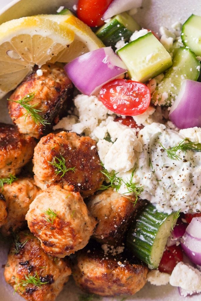 close up shot of meatballs with greek salad and tzatziki sauce
