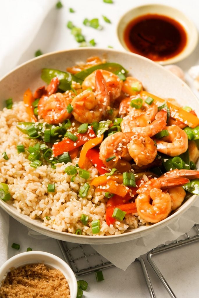 teriyaki shrimp stir fry in a bowl with brown rice, sesame seeds, and green onions