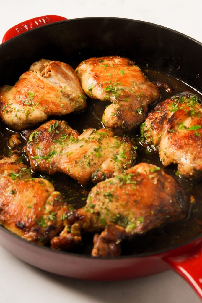 seared chicken thighs in a skillet with chicken broth, fresh herb, and butter